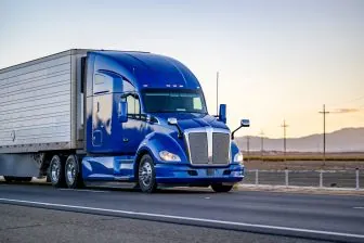 blue semi truck driving down highway at sunset resize1