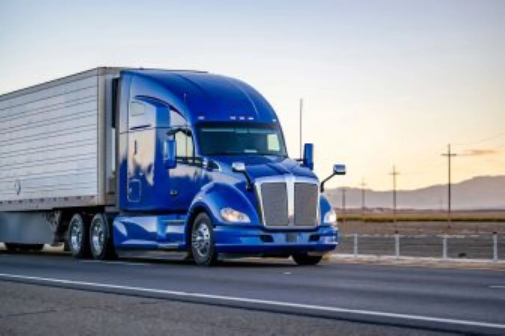 blue semi truck driving down highway at sunset resize2