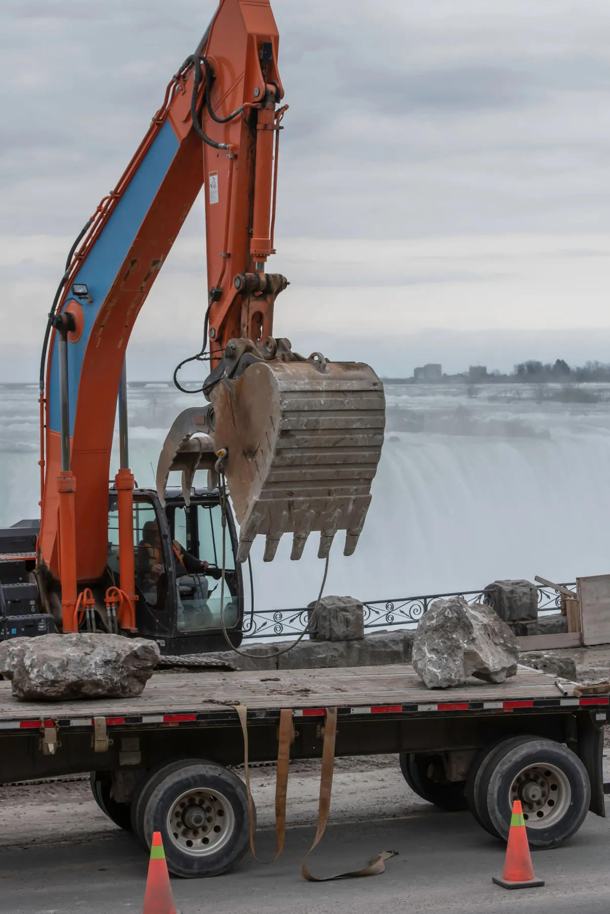 An excavator unloading large rocks from a flatbed trailer