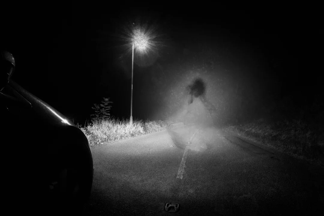 America's Haunted Highways an illusion of a girl in white dress on a dark rural road with car headlight casting light upon her