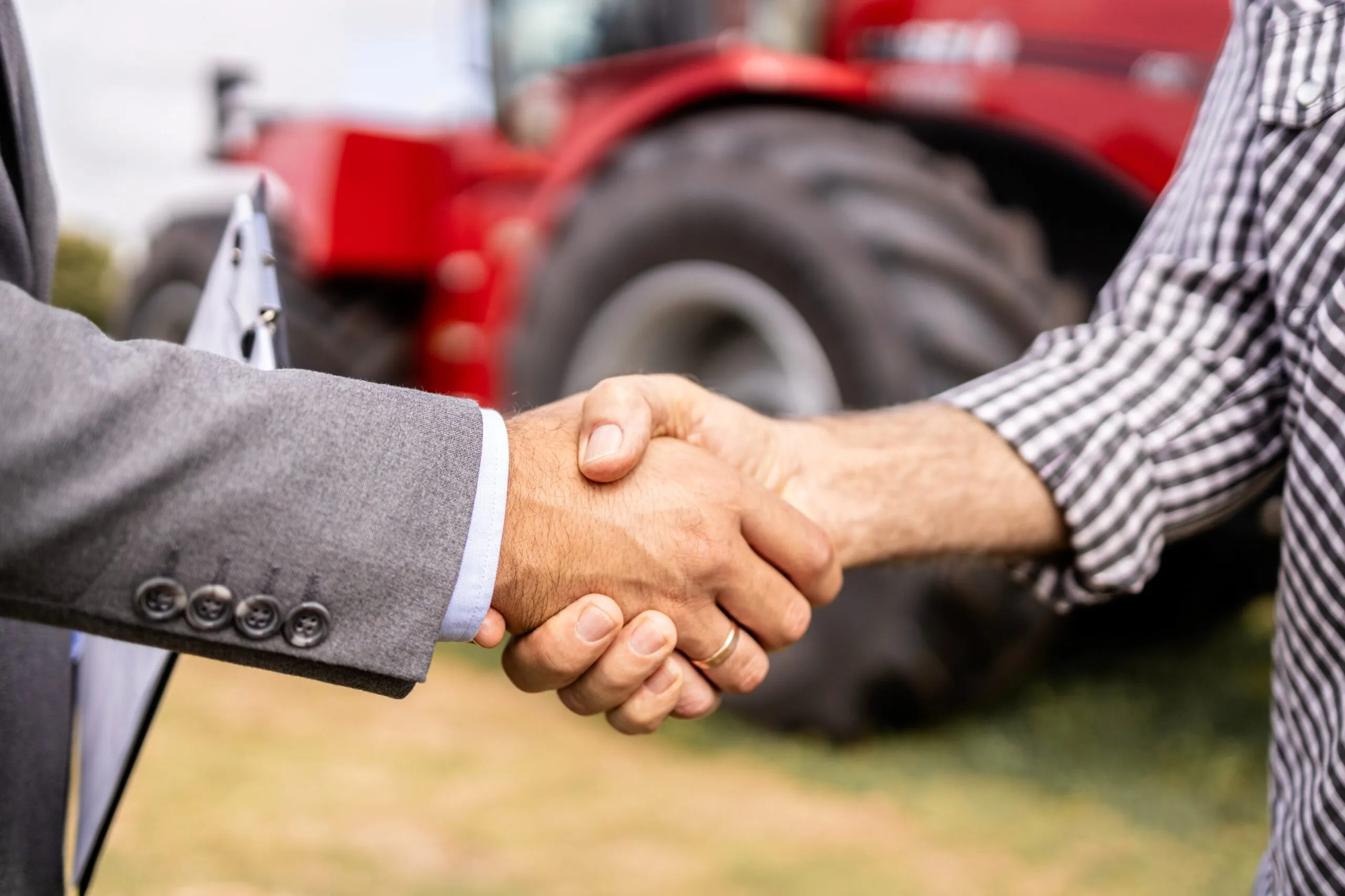 business man and shipper shaking hands tractor in background