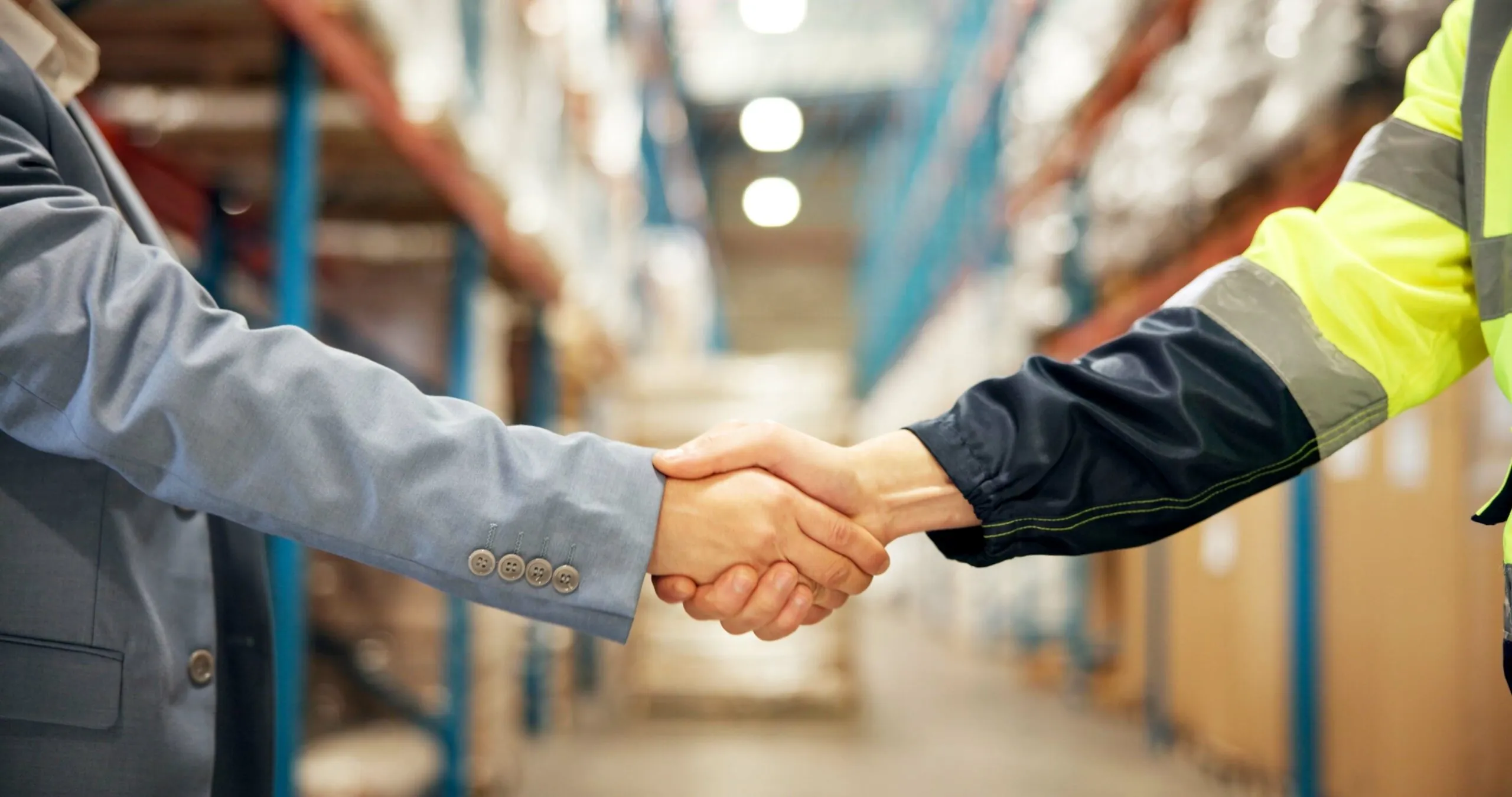 business person and logistics person shaking hands in warehouse