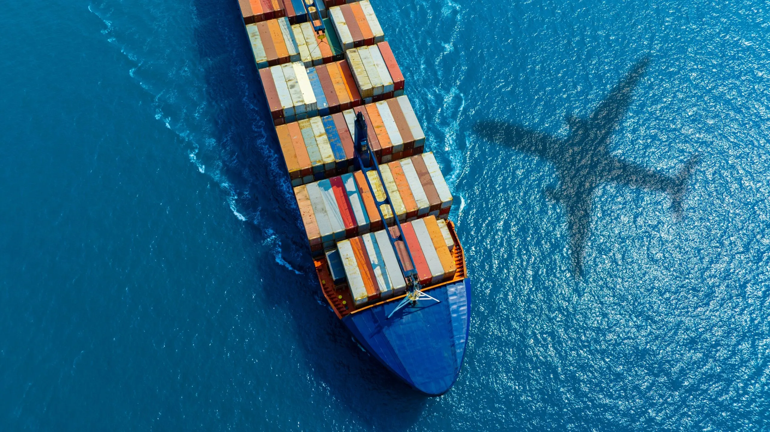 cargo ship on ocean and airplane shadow over water