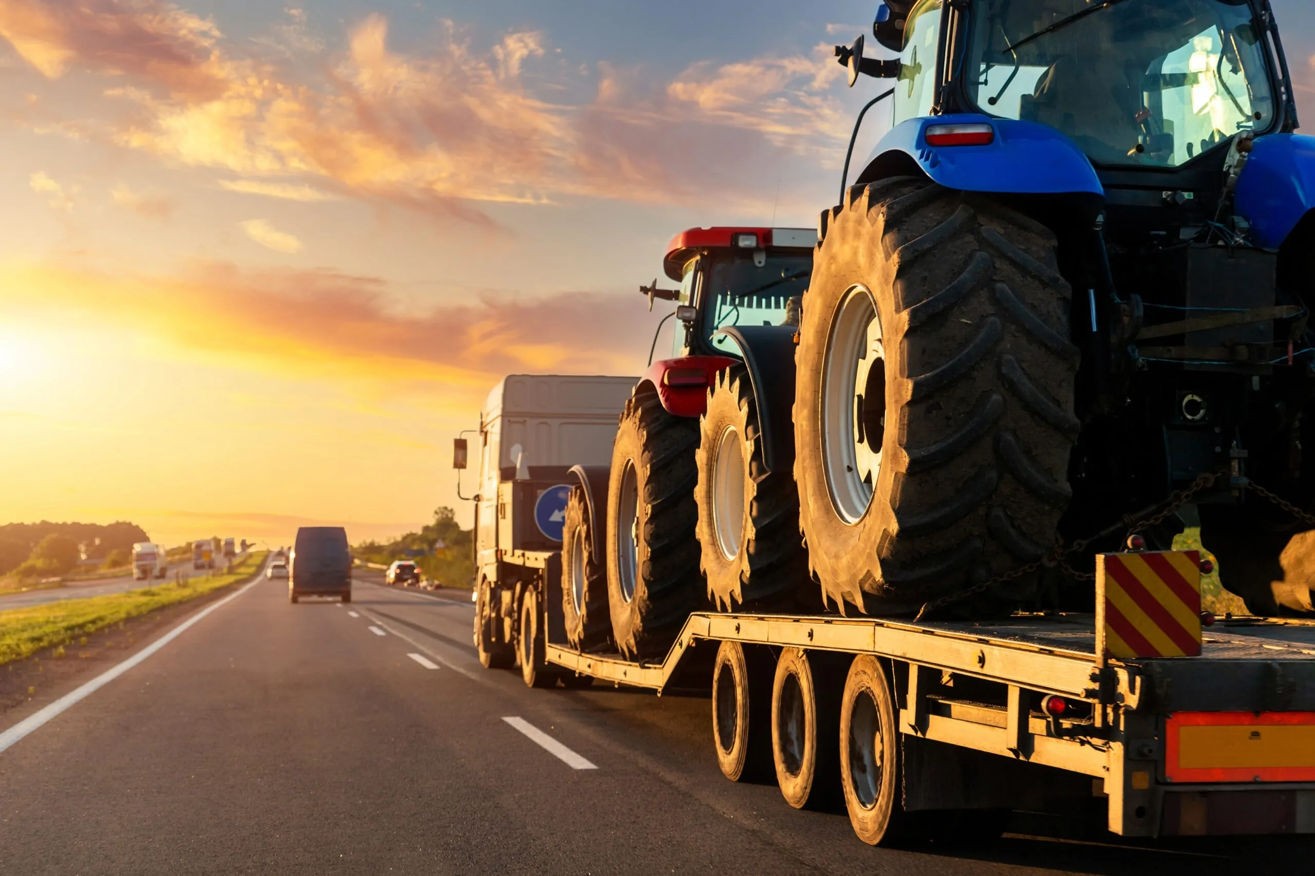 flatbed carrying two tractors driving on highway, agricultural equipment