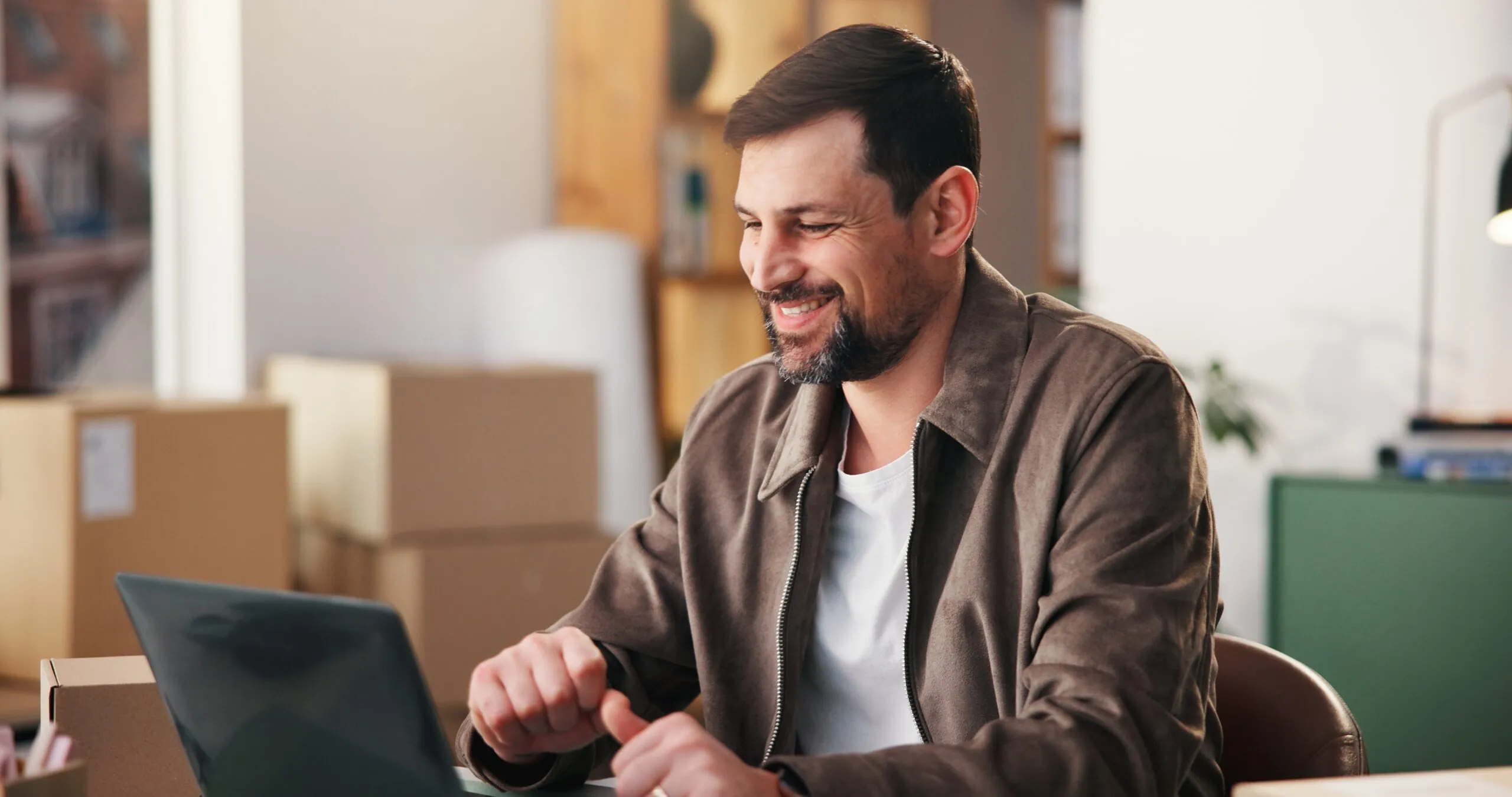 man laughing at computer in office with boxes behind on floor, improve smb shipping