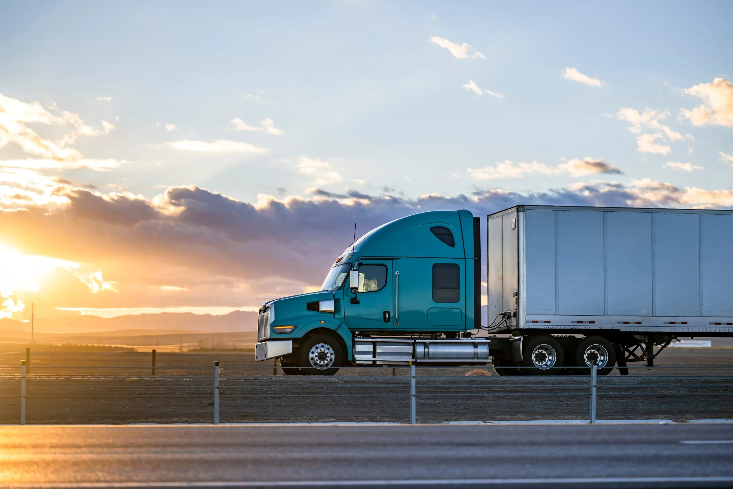 semi truck driving down highway at sunset