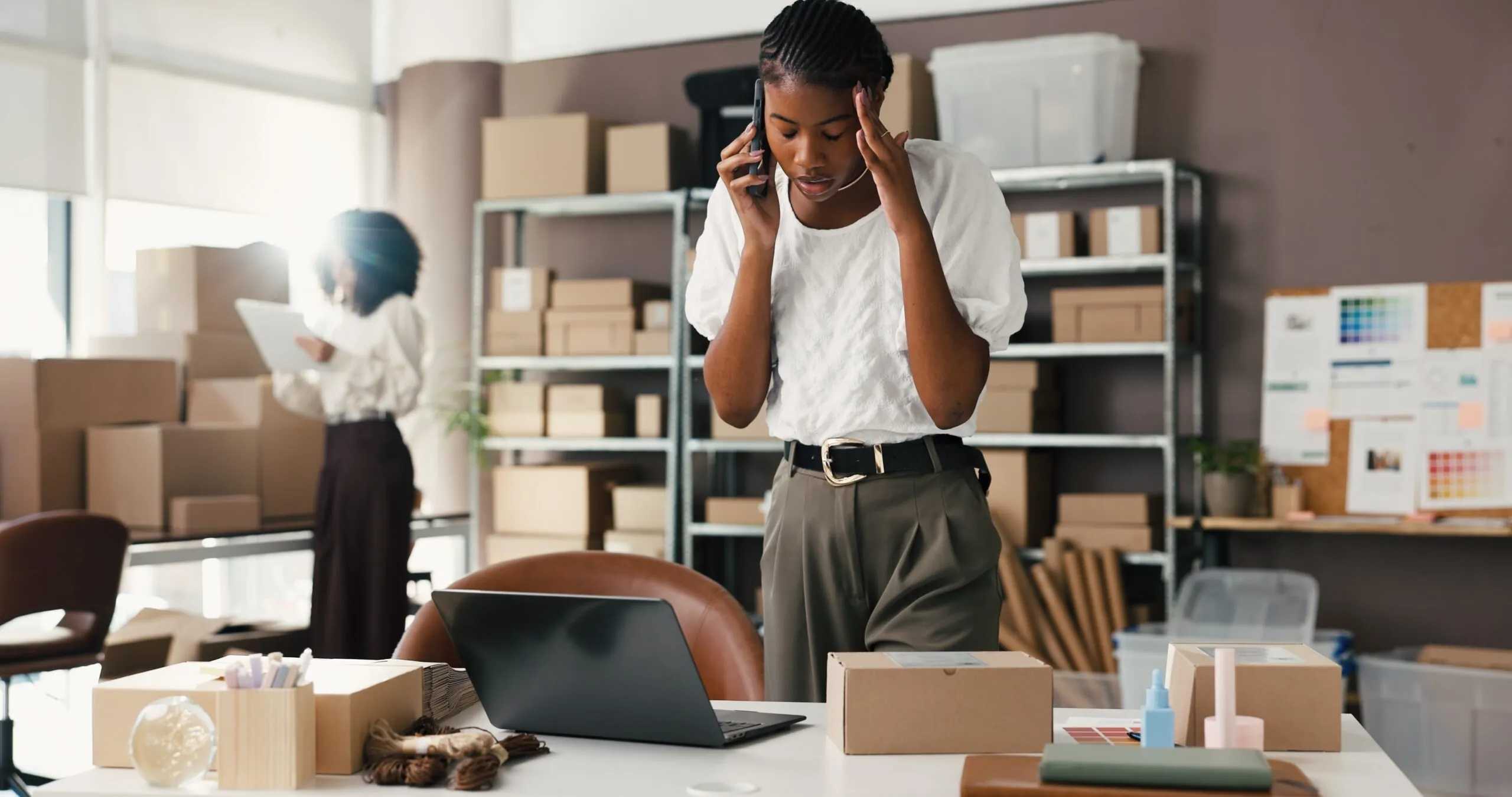 stressed woman on phone standing in office with boxes, business shipping mistakes