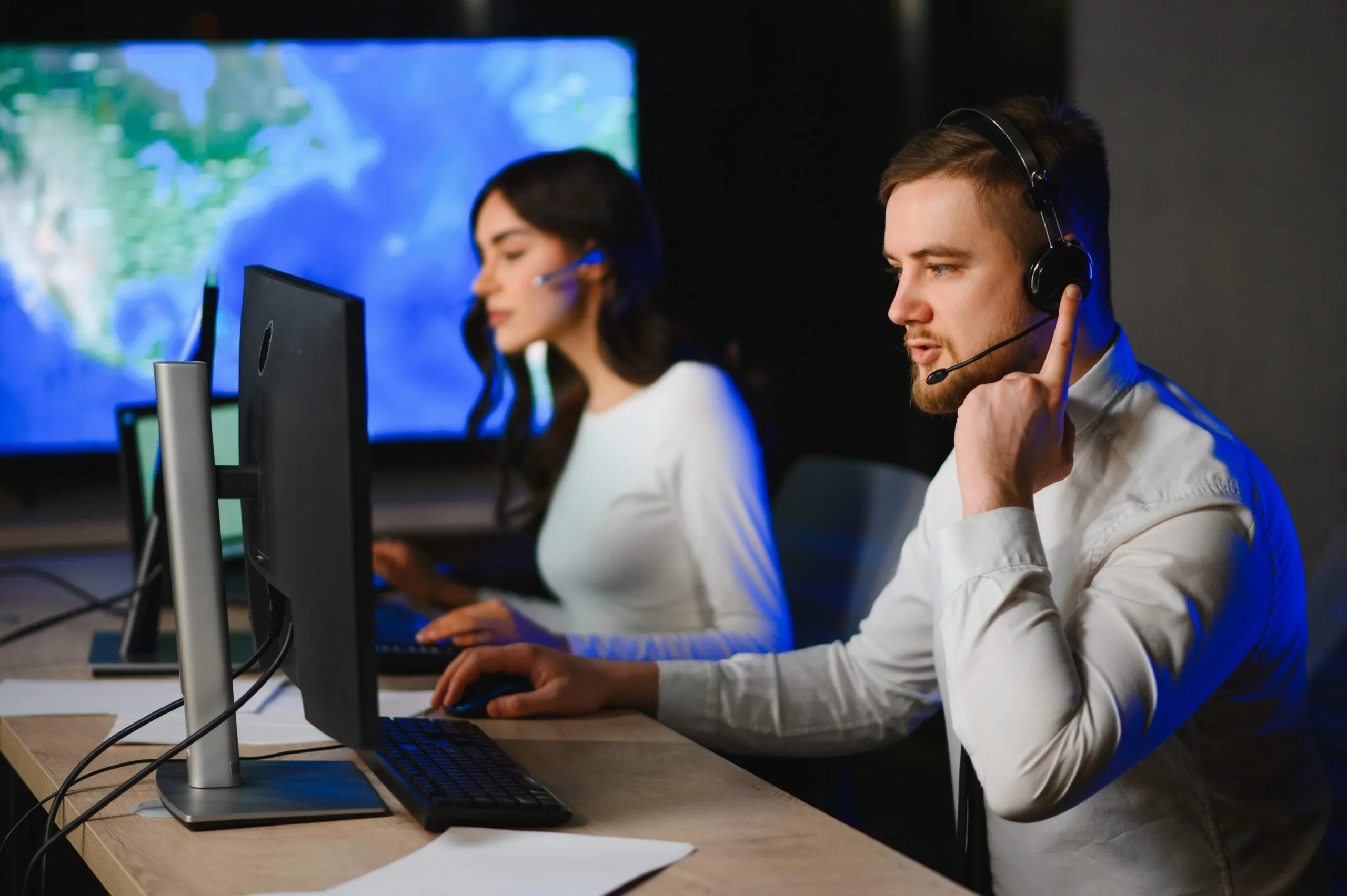 two workers sitting at computers with headphones on work calls