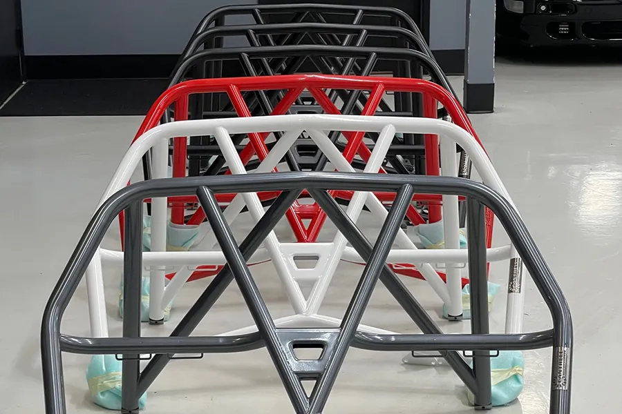 A line of multiple red white and black roll bars for racing vehicles in a auto shop