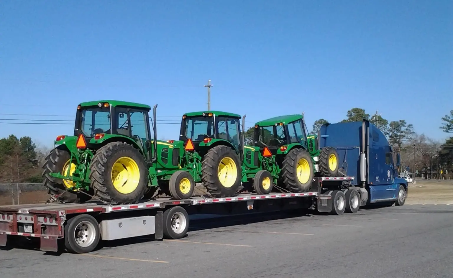 3 tractors being shipped on the back of a flatbed freight truck