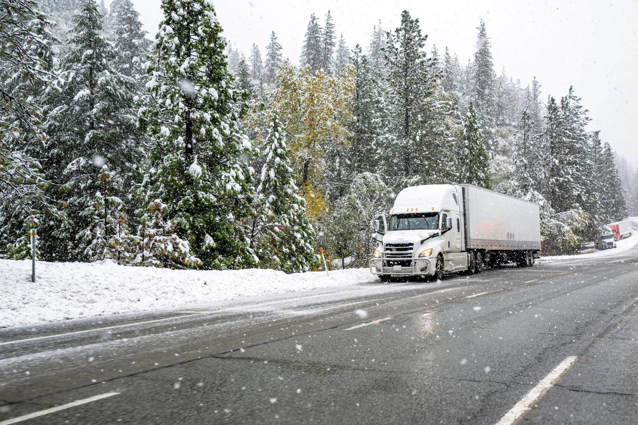 semi truck driving on forest road as snow falls