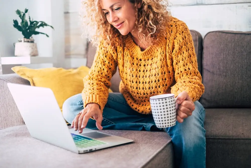 lady with blonde curly hair on laptop sitting down on the sofa at home check online shops for cyber monday sales