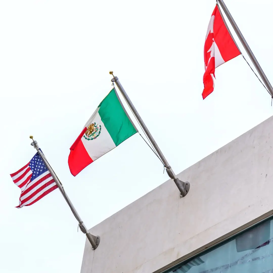 three flags of US Mexico and Canada on flagpoles on building