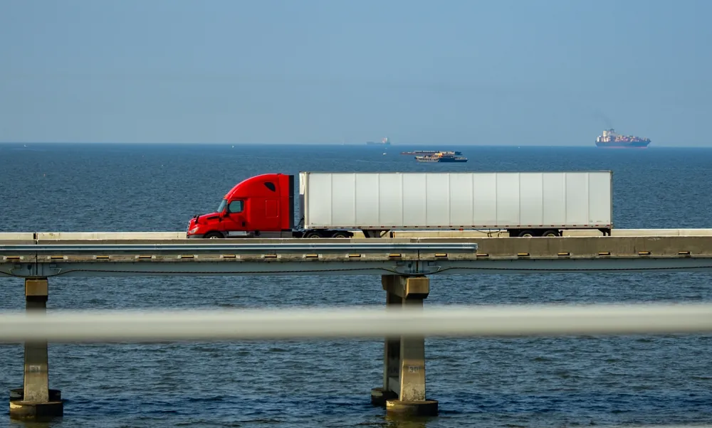 Summer Shipping Tips red semi trailer truck driving on a bridge over ocean