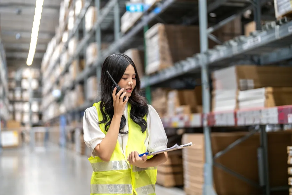 Summer Shipping Tips warehouse workers confirming shipment details on her clipboard and sharing it on walkie-talkie
