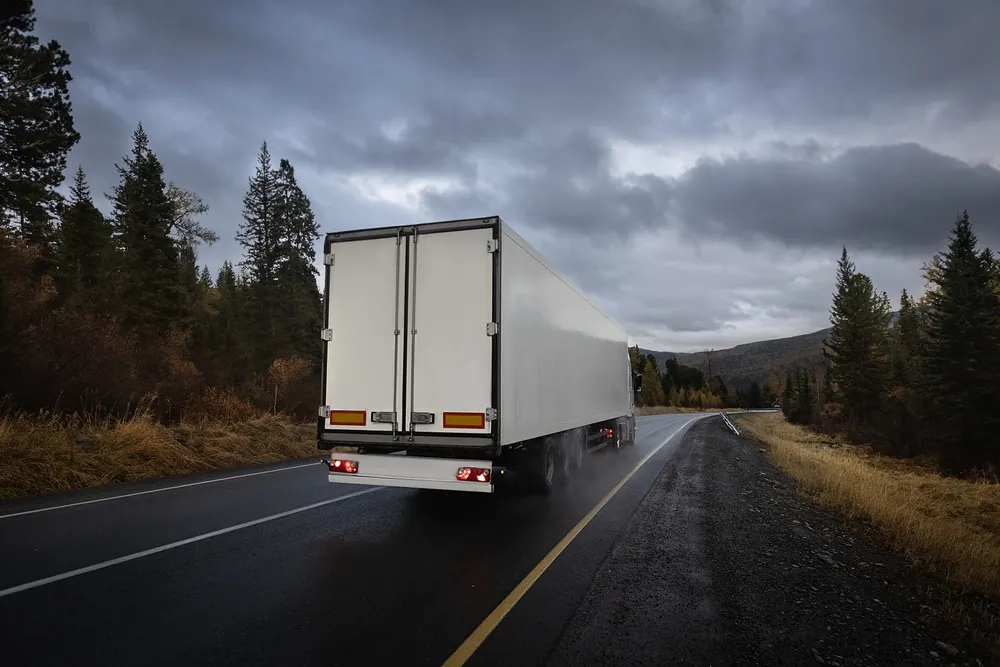Summer Shipping Tips white semi trailer driving down rural highway on a dark and stormy evening