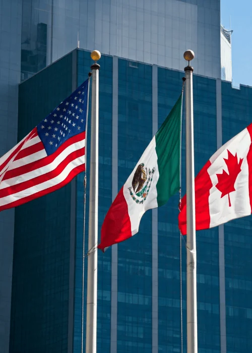 three flags of US Mexico and Canada on flagpoles Infront of building
