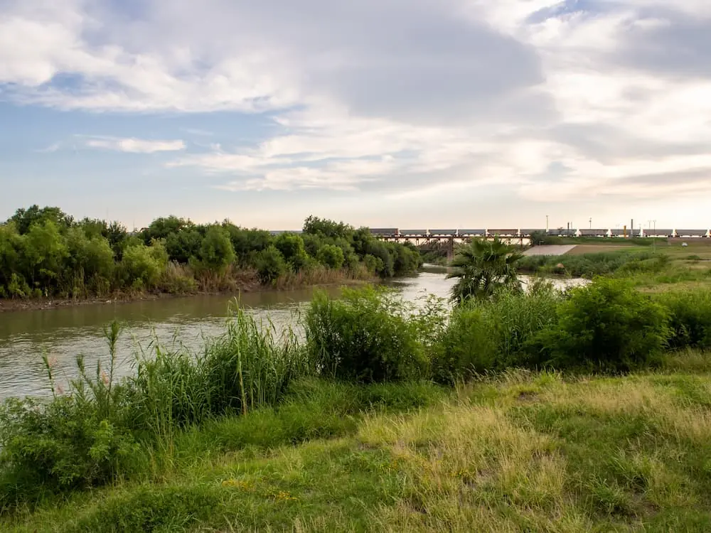 Industry News March 2026 distant view of freight train crossing border between USA and Mexico via bridge over riverbank