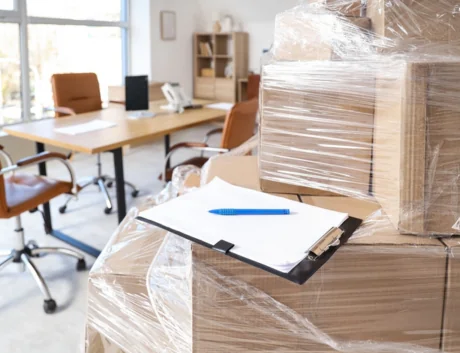 Wrapped cardboard boxes with stretch film and clipboard in office on moving day