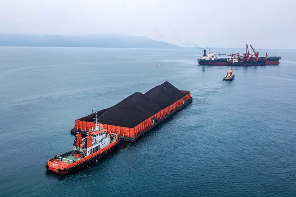 tugboat pushing barge filled with coal towards a floating barge ship near an island