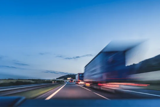 Five Reasons to Use Expedited Freight Shipping trucks speeding down rural highway in the evening PREVIEW VERSION