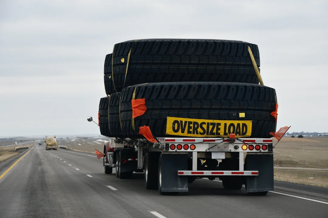 Special Requirements When Shipping Freight jumbo tires stacked on flatbed trailer with a yellow oversize load sign on the backside driving down highway