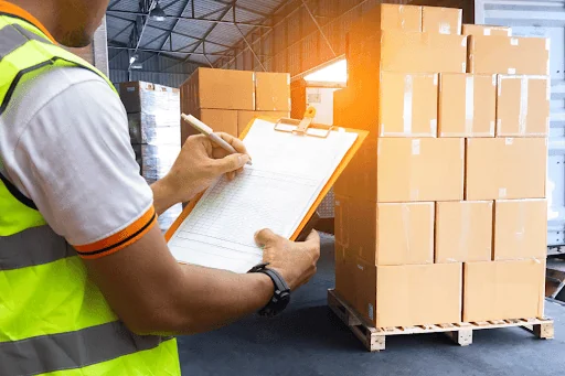 A worker checking of a list on a clipboard in front of boxes