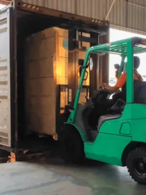 Forklift Tractor loading package boxes into shipping container at dock warehouse