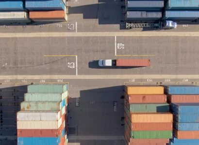 AERIAL, TOP DOWN: White truck transports a red freight container across the busy port