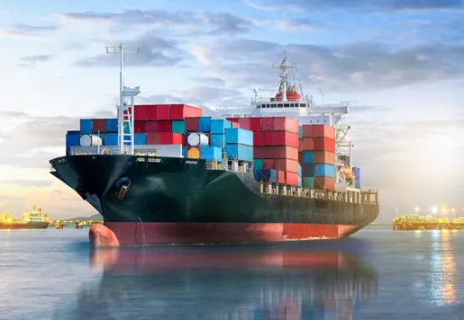 Cargo ship loaded with multicolored shipping containers sailing in a harbor at sunset