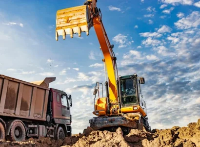 A wheeled excavator loads a dump truck with soil and sand