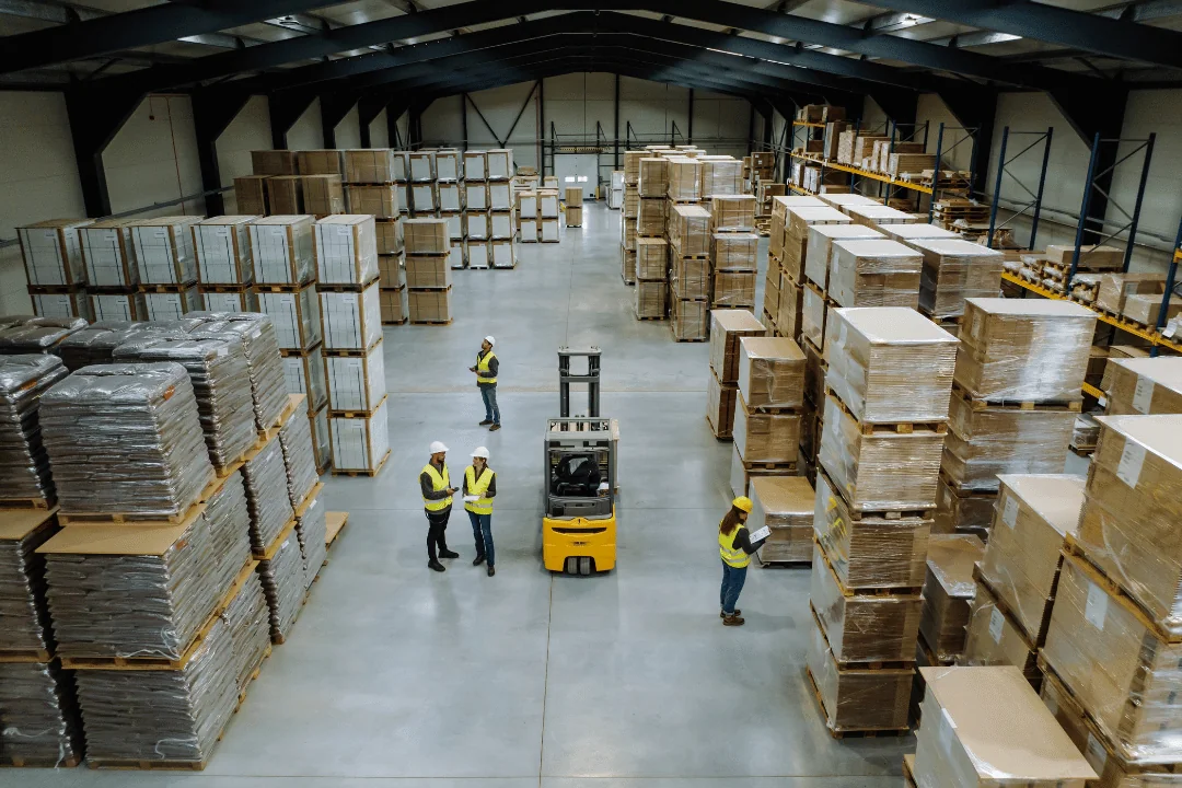 Party logistics from 1 to 5 aerial view of workers in a warehouse full of palletized packages with a forklift in the center of the floor
