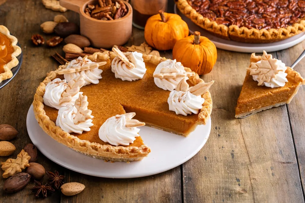 The Supply Chain Behind Thanksgiving Staples pumpkin and pecan pies on a wooden table with decorative pumpkins in between them