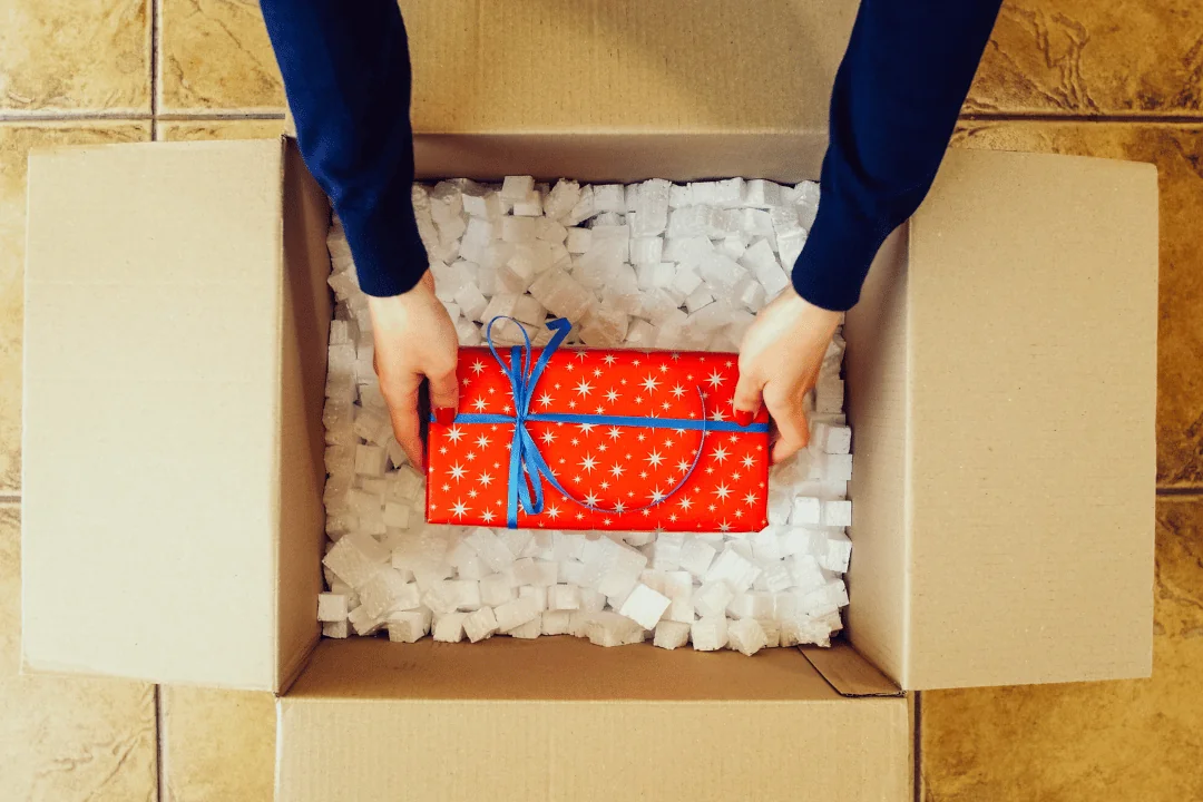 woman putting present inside cardboard box with Styrofoam peanuts inside