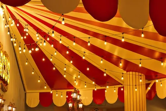 Freight Shipping Circuses a circus sign inside of a yellow and red big-top tent illuminated by bulb string lights and vintage lamp posts PREVIEW VERSION
