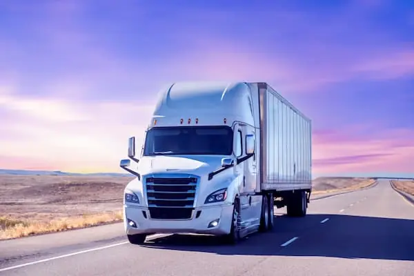 The Spring Break Effect white semi trailer truck driving down desert highway during a pink and blue sunrise