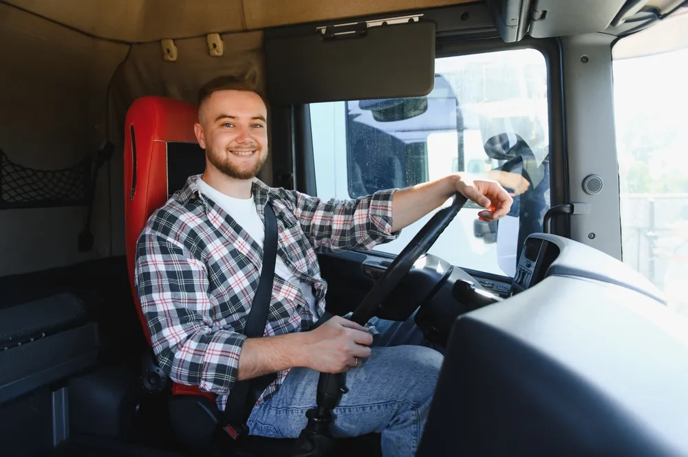 Truck Driver Mentorship truck driver smiling at camera as he is buckled into his seat and ready to drive