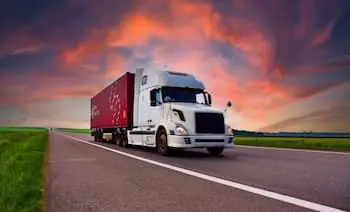 Truck Driver Mentorship white semi trailer hauling a red shipping container drives down road during sunset PREVIEW VERSION