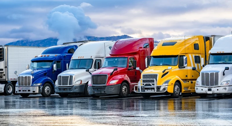line up of different color semi trucks parked at a rest stop