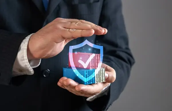 How to Protect Your Shipment in Unprecedented Times person holding up toy shipping containers while a shield symbol hovers in front of them