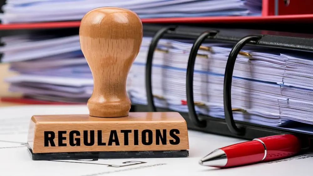 The Rise and Fight Against Chameleon Carriers wooden stamp labeled Regulations next to a heavy binder and pen