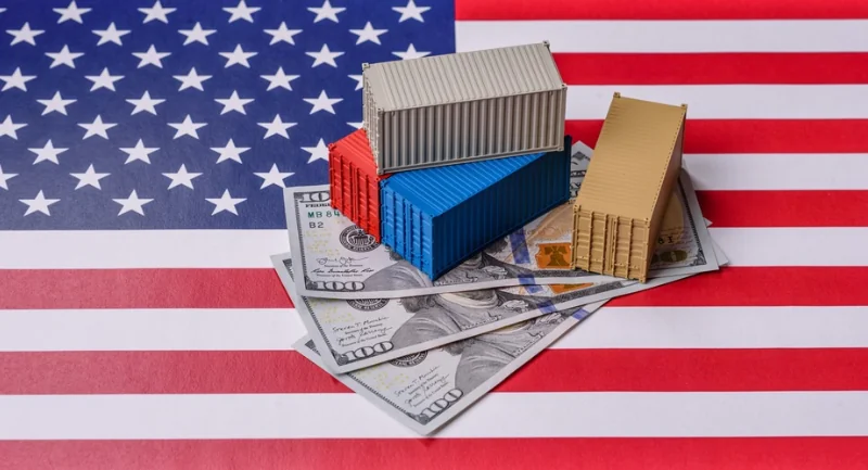 multi colored model container ships sitting on top of 100 dollar bills all on top of an American flag