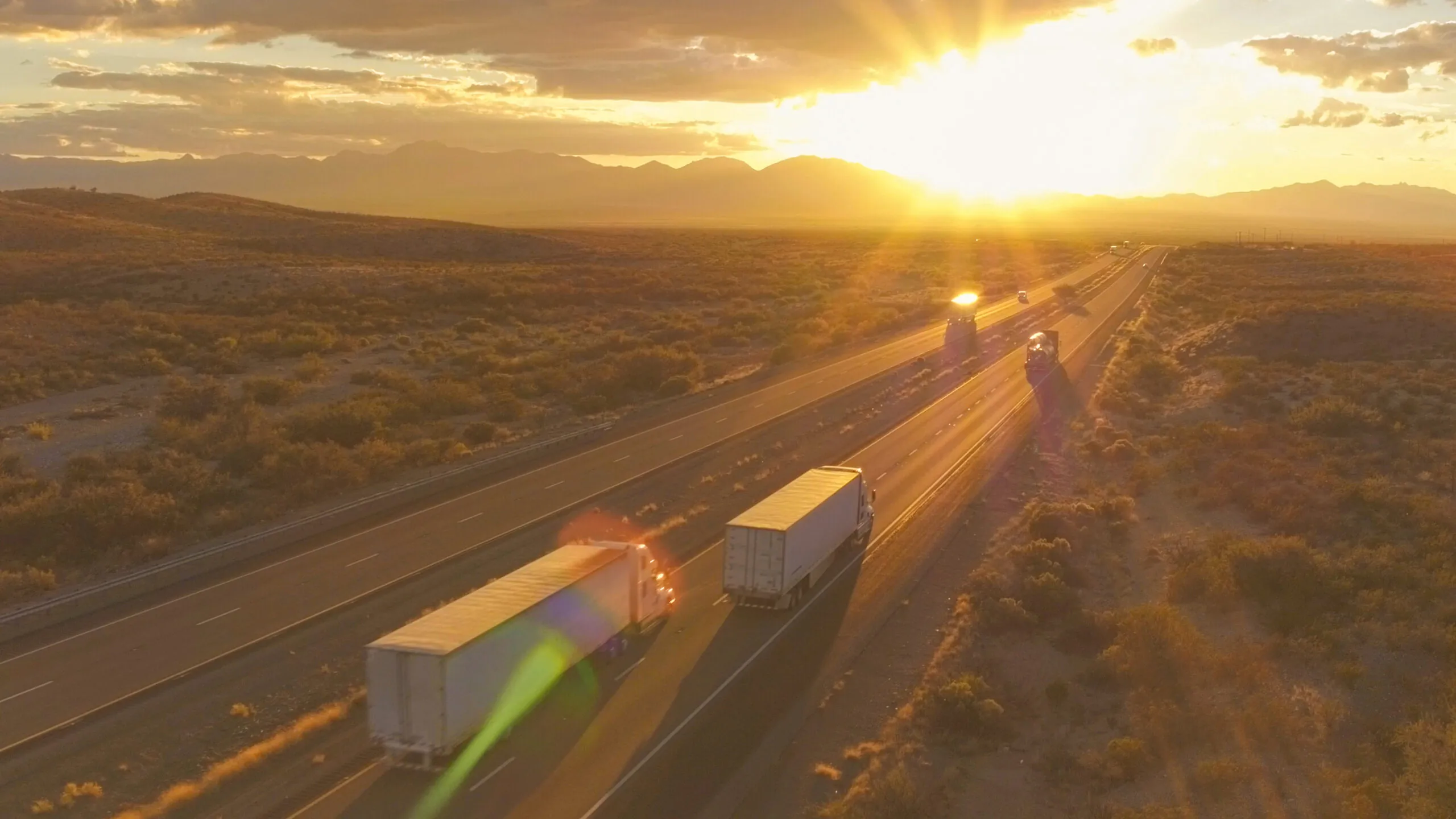 trucks driving down a highway towards the setting sun