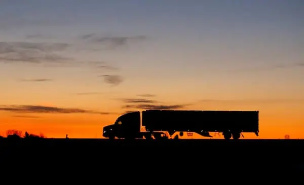 American freight truck driving down road at sunset