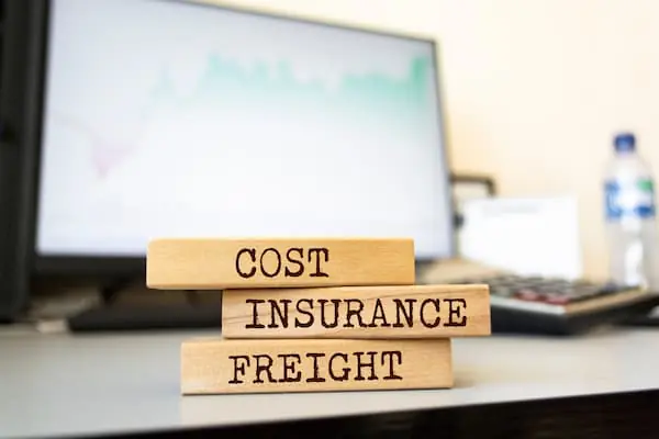 long wooden blocks with the words Cost Insurance Freight on them in front of a laptop showing freight data