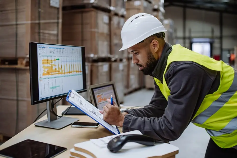 Distribution Centers vs Warehouses worker reviewing data on his computer and on the paper in his hand