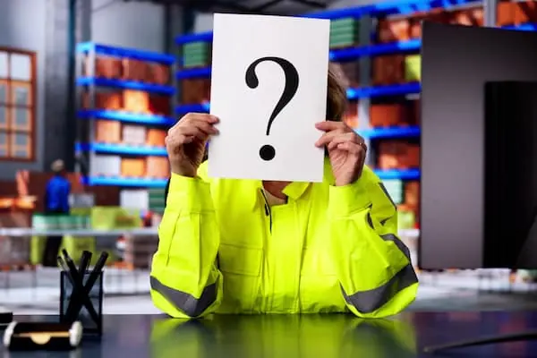Seasonal Hiring Models warehouse worker sitting at desk in the middle of the warehouse floor holding a paper with a question mark over face