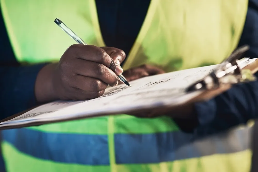close up of worker with vest writing on clipboard