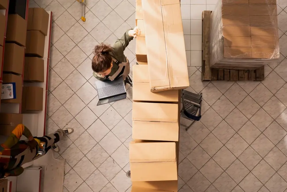 Harsh Reality of the Modern Freight Recession topdown view of workers in a small warehouse organizing inventory on shelves that arrived on pallets