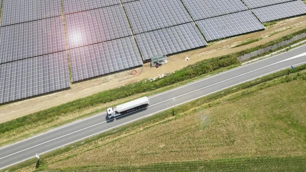 What Would Logistics Look Like If Fuel Ran Out aerial view of a white semi trailer driving past a solar panel farm on a sunny day